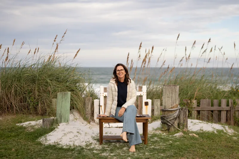 Jill Futrell sitting on a wooden bench at a beach dune crossover