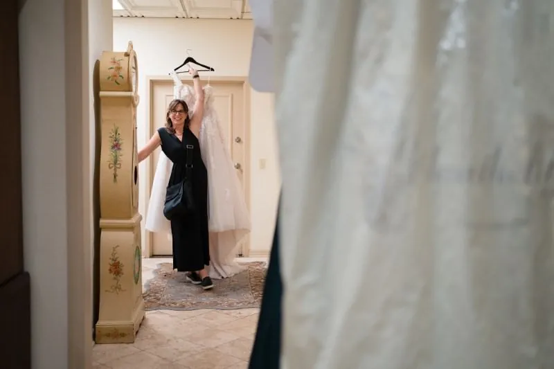 Jill Futrell triumphantly holding up a wedding dress on a hanger