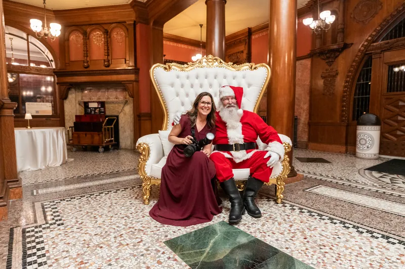 Jill Futrell with her camera, sitting beside Santa in a hotel lobby