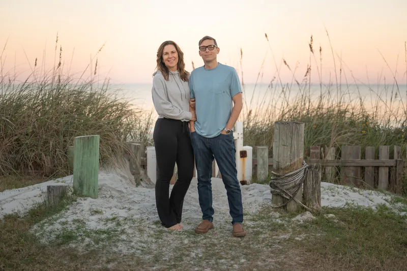 Rob and Jill Futrell standing together on the beach at sunset among the sea oats