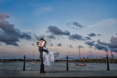 Groom lifts bride on bayfront with Bridge of Lions at sunset