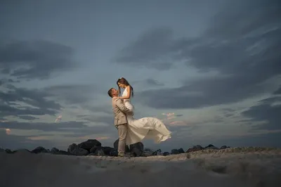 Groom lifts bride on St Augustine beach with dramatic sky