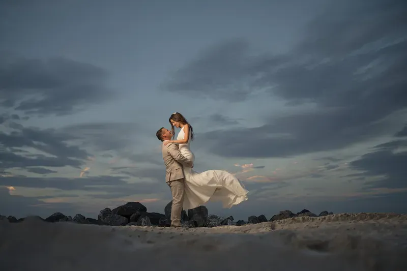 Groom lifts bride on St Augustine beach with dramatic sky