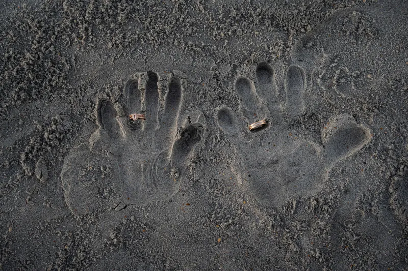 Wedding ring detail shot with hand prints in sand