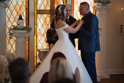 Couple exchanging rings at chapel ceremony with stained glass backdrop