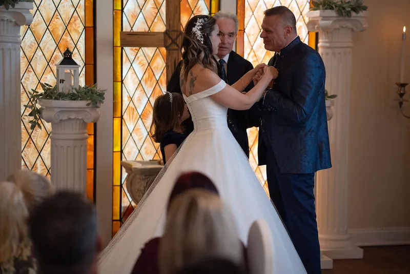 Couple exchanging rings at chapel ceremony with stained glass backdrop