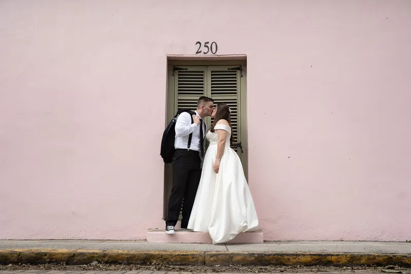 Couple kissing by pink wall with green shutters in historic district