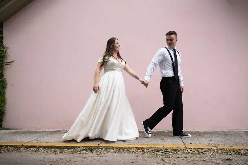 Couple walking hand in hand by pink wall in St Augustine
