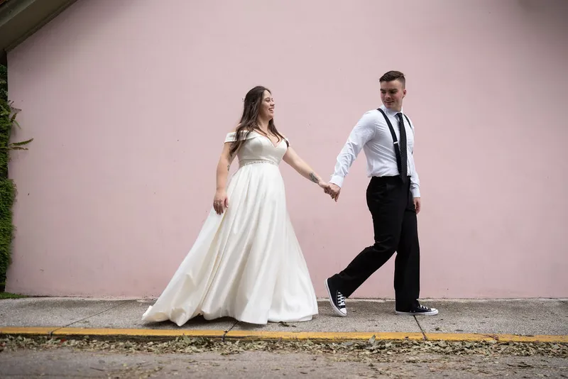Couple walking hand in hand by pink wall in St Augustine