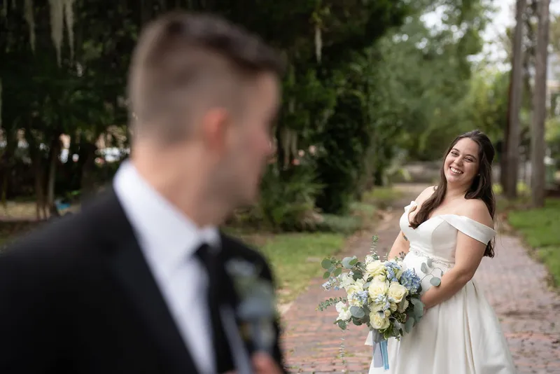 First look moment with bride laughing on brick path with Spanish moss