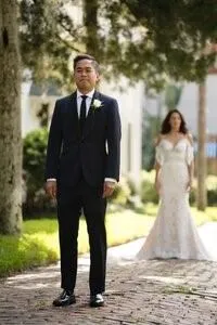 First look moment with groom waiting as bride approaches on brick path