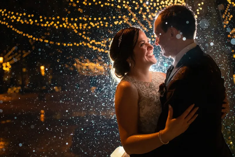Couple kissing in rain during Nights of Lights with string lights