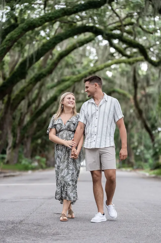 Abby and Gage walk hand-in-hand down a tree-lined street on Magnolia Avenue, with massive oak branches creating a natural