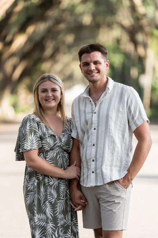 Abby and Gage smile at the camera while walking together under oak tree canopies on Magnolia Avenue, holding hands.