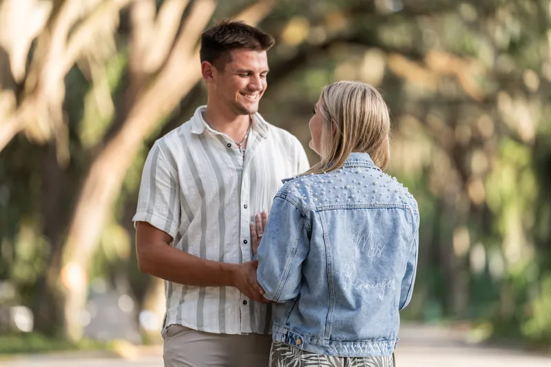 Gage and Abby stand under sprawling oak trees on Magnolia Avenue, holding hands and smiling at each other in dappled