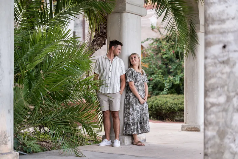 The couple stands side by side beneath ornate arches at The Loggias, framed by verdant palms and classic architectural