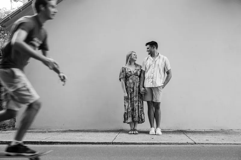 A black and white image captures Abby and Gage standing together against a white wall as a blurred figure passes