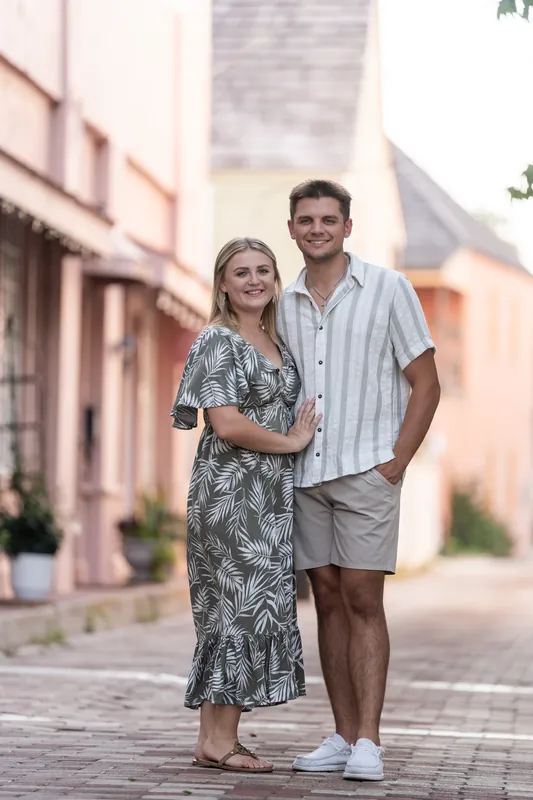Abby links her arm through Gage's as they walk down a soft pink-washed street lined with historic architecture.