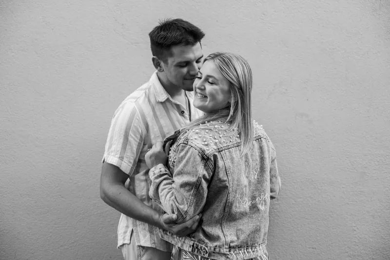 In a black-and-white portrait, Gage wraps his arms around Abby from behind as she gazes toward the camera.