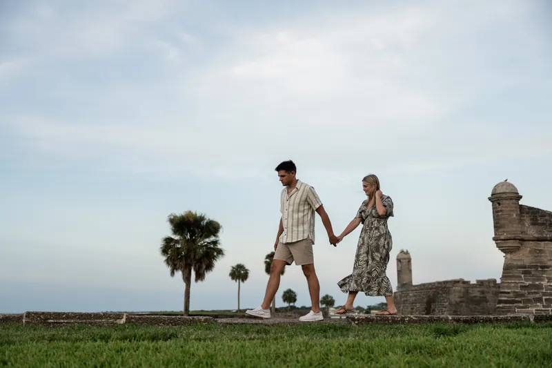 Holding hands, Abby and Gage walk across the grassy grounds with the fortress and palmetto trees framing the scene.
