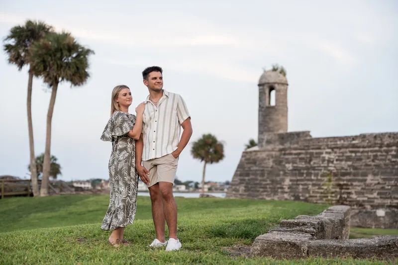Abby in a floral dress leans against Gage in his striped shirt as they pose near the fort's watchtower.