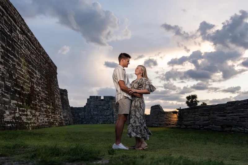 Abby and Gage stand together at the Castillo de San Marcos with dramatic evening clouds above the historic stone fort's