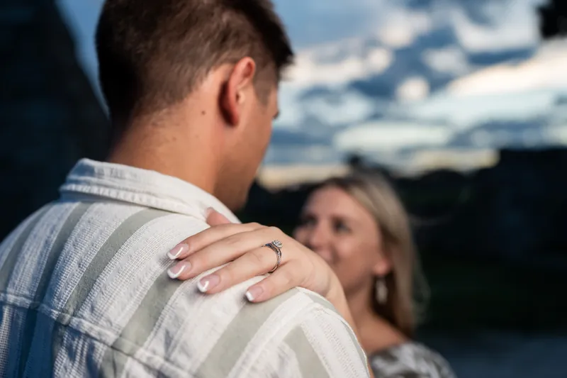 Gage's hand rests on Abby's shoulder as she gazes upward, their profiles backlit against the fort's weathered walls and sky.
