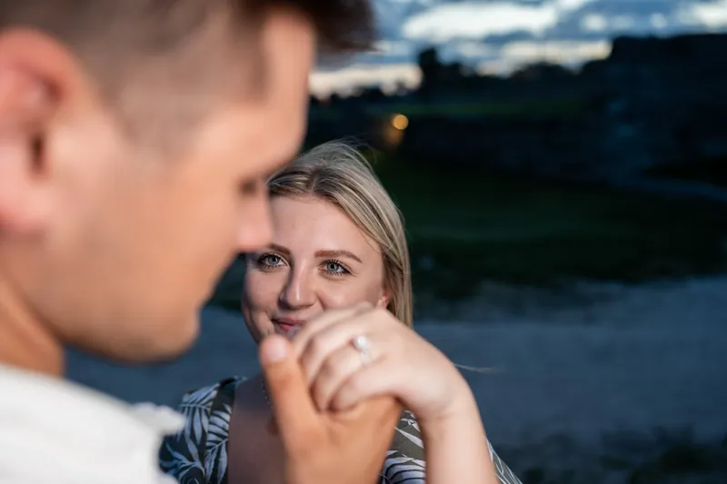 Abby smiles at Gage while holding his hand, the stone fortress visible softly behind them in evening light.
