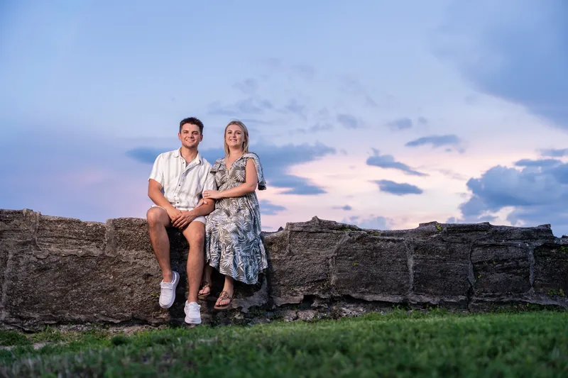 The couple sits on the fort's ancient cannon wall as dusk settles over the grassy grounds and cloudy horizon.