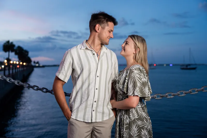 Gage and Abby face each other at the St. Augustine Bayfront at dusk, with moored boats and lit docks visible across the water