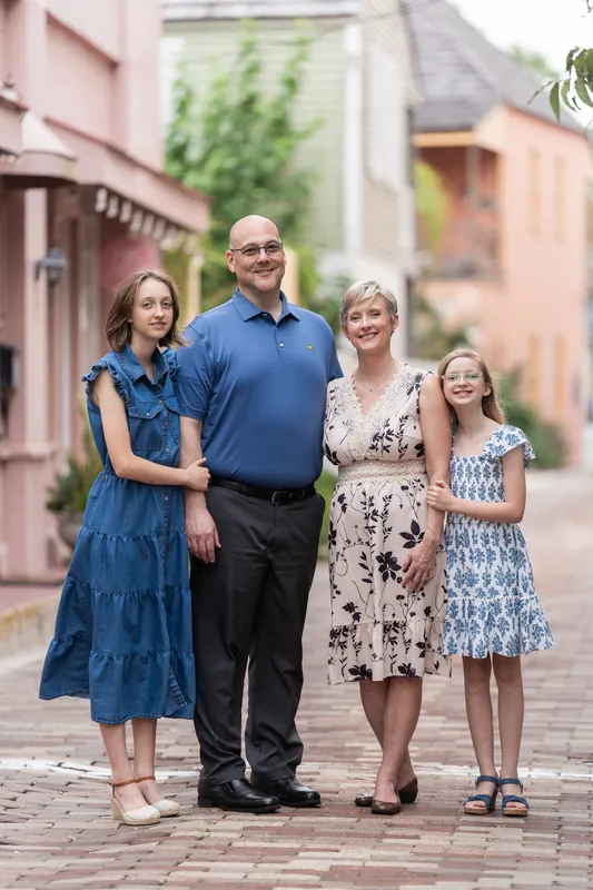 Two adults and two children stand on a brick street with soft-colored historic buildings behind them in Downtown St Augustine.