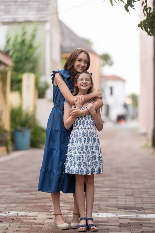 Two people in dresses embrace while standing on a brick pathway lined with colonial architecture in Downtown St Augustine.