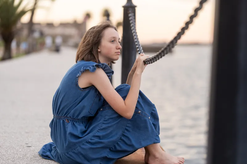Someone in a blue dress sits on a brick Downtown St Augustine street, gazing over their shoulder toward the waterfront.