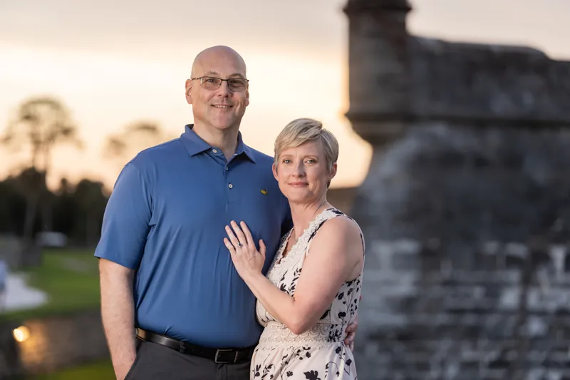 Two adults embrace near a waterfront fortification, silhouetted against the golden sky at Downtown St Augustine.