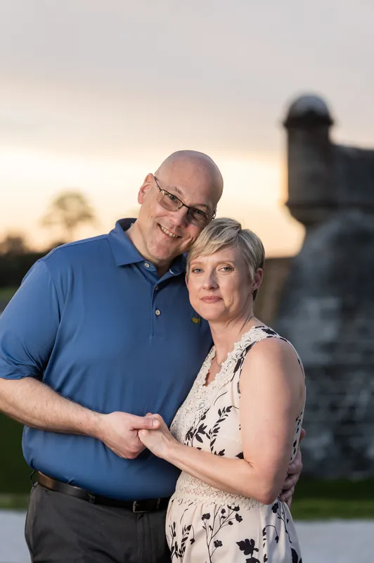 A couple holds each other close as the sun sets behind a historic tower at Downtown St Augustine.