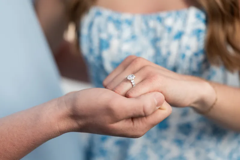 Close-up of Teigan's hand showing her diamond solitaire engagement ring as she rests her hand on Alex's.