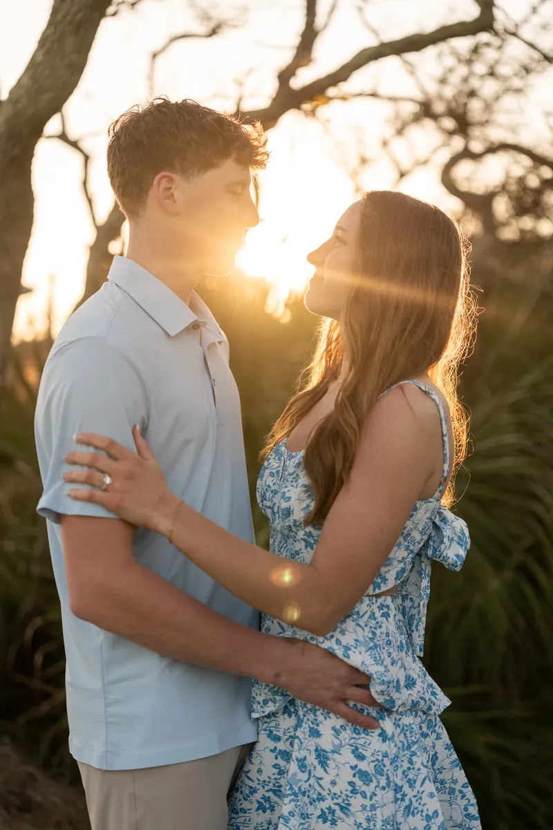 Alex and Teigan embrace under a gnarled tree with warm sunlight filtering through the branches.
