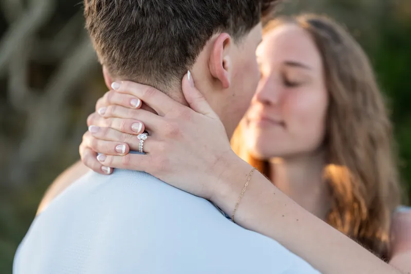 Teigan hugs Alex from behind, showing off a diamond engagement ring on her left hand.