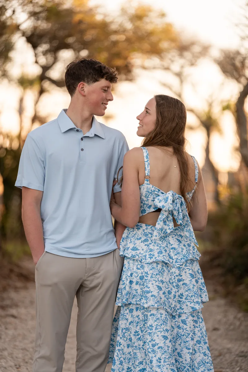 Teigan looks back at Alex while they stand together on a wooded path with dappled sunlight filtering through the trees.