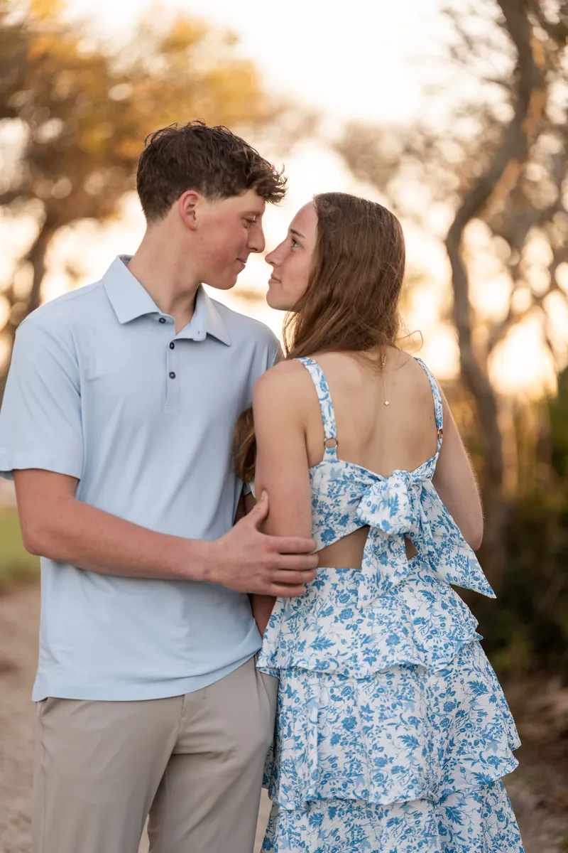 Alex and Teigan stand close together on a dirt path, with Alex's arm around Teigan's waist as they look at each other.
