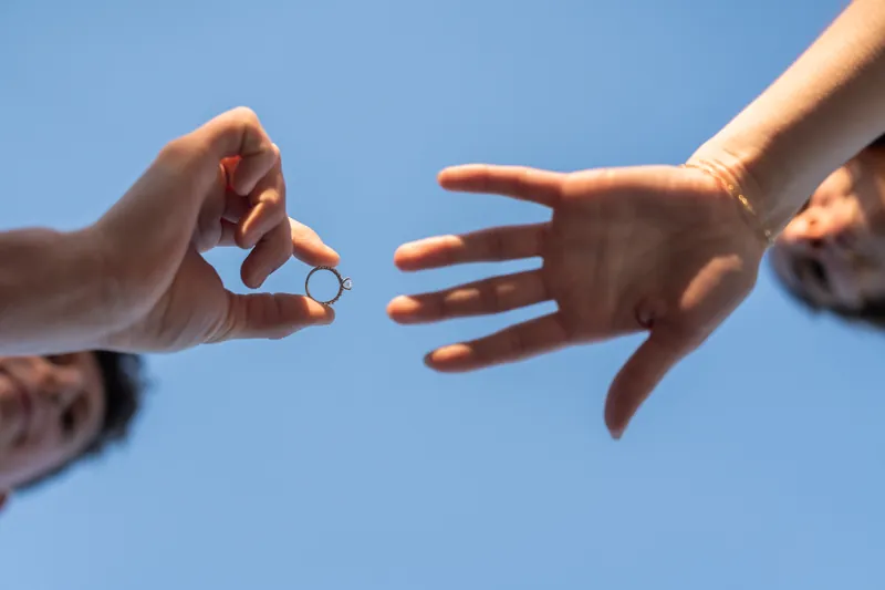 Teigan's hand holds Alex's hand against a clear blue sky during their proposal.