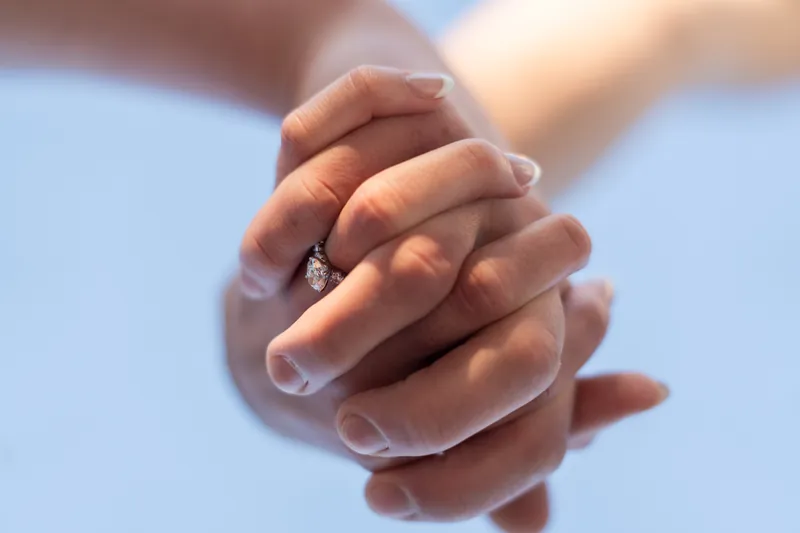 Alex and Teigan's joined hands display the engagement ring with a clear sky backdrop.