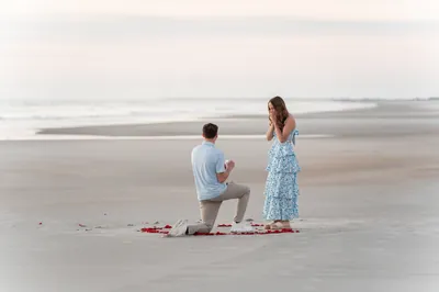 Man proposing on beach with ring, St. Augustine proposal photographer captured romantic moment with woman in blue dress on sandy shore