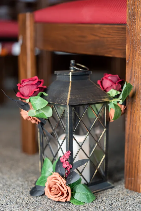Coral and blush roses tied with greenery adorn a black metal lantern with glass panes.