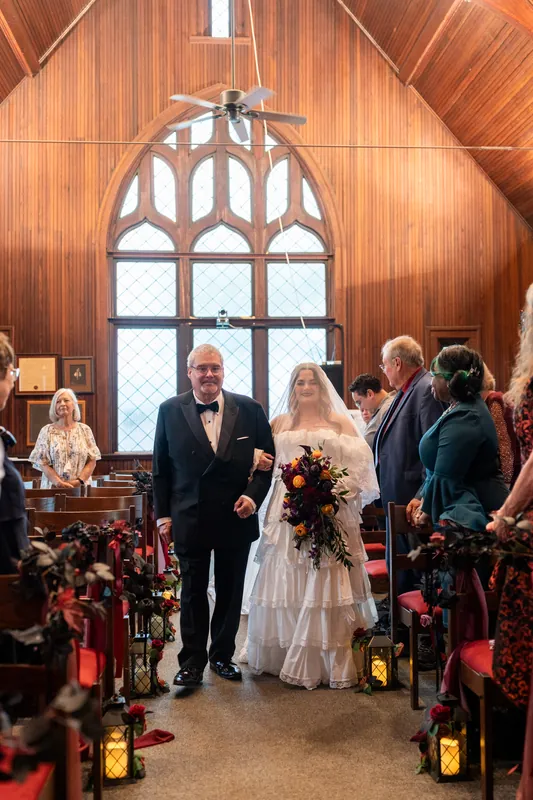 Jason and Alexandra walk down the aisle at Riverhouse Events beneath a dramatic peaked wooden arch.