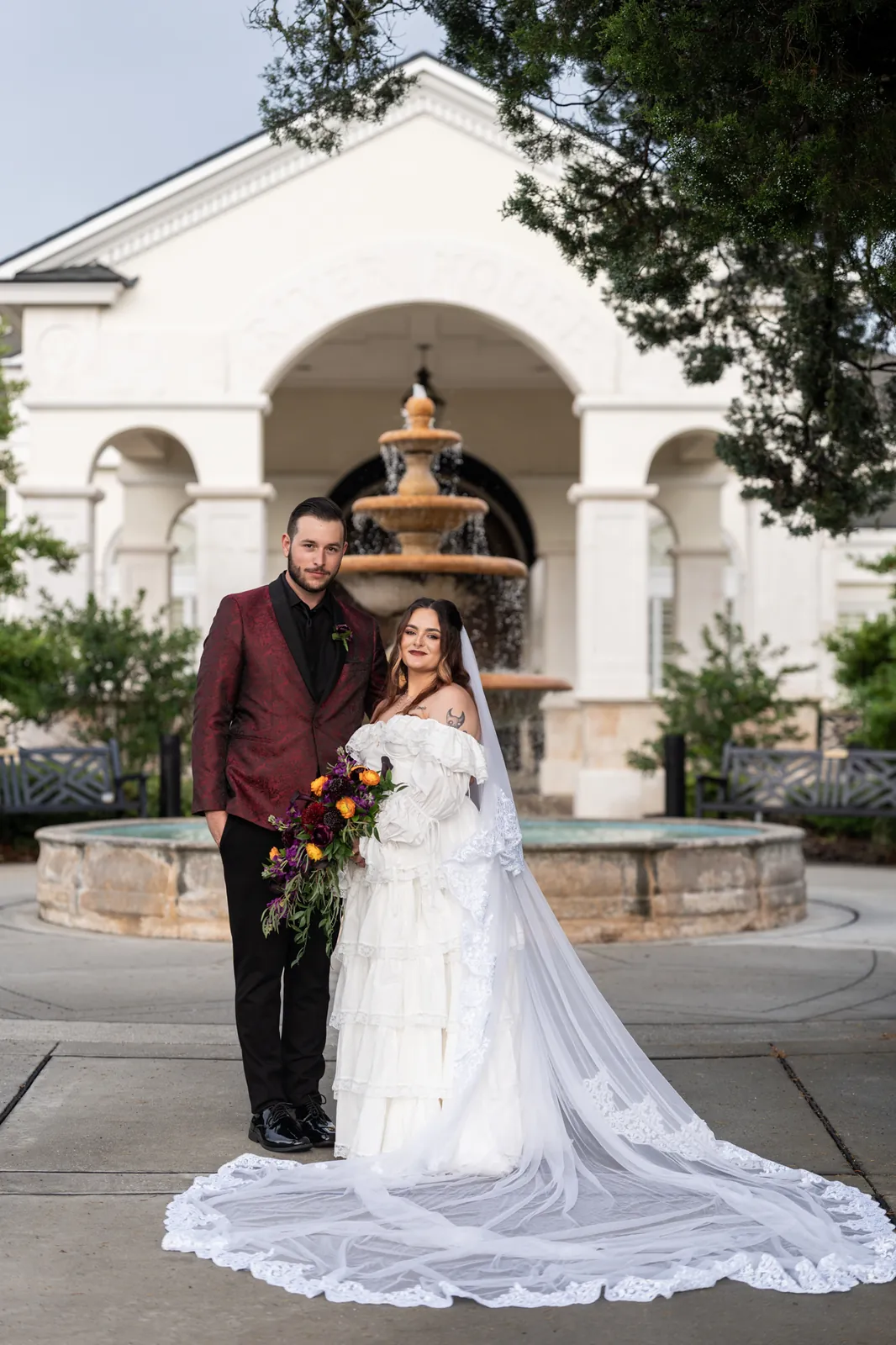 Jason in burgundy and Alexandra in white embrace before the arched fountain at River House Events, St. Augustine.