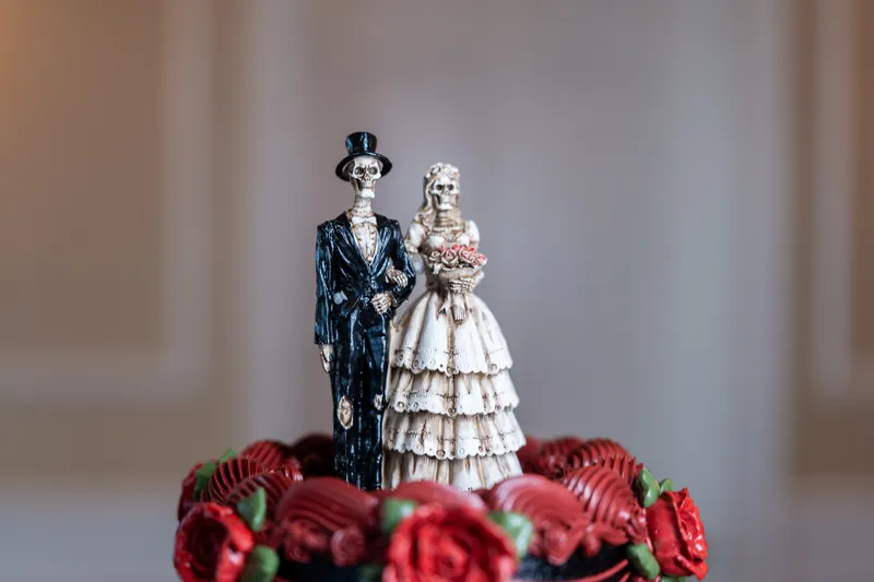 Ornate bride and groom cake toppers stand atop red roses on the tiered wedding cake at Riverhouse Events.