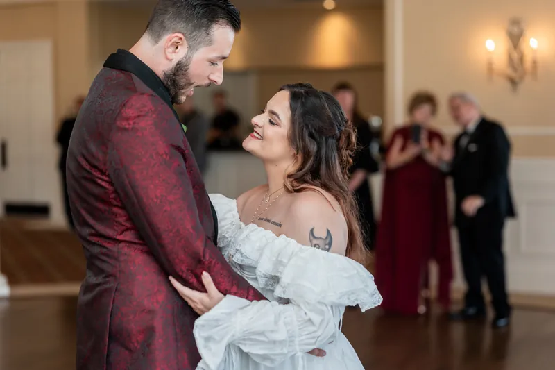 Jason and Alexandra dance closely during their first dance at Riverhouse Events, her white dress flowing as they gaze at each other.