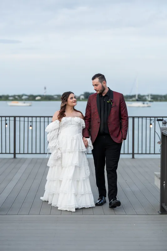 Alexandra and Jason walk hand-in-hand across the wooden deck at Riverhouse Events, overlooking the water.
