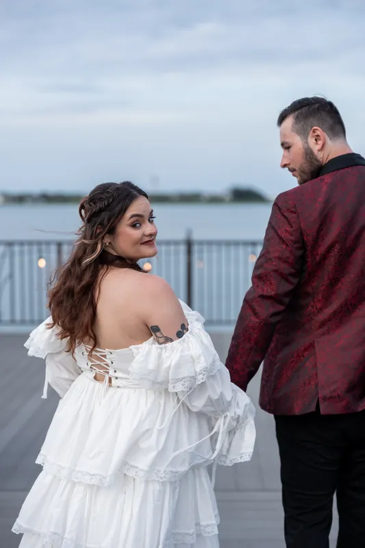 Alexandra gazes back over her shoulder while standing beside Jason on the riverside deck at Riverhouse Events.